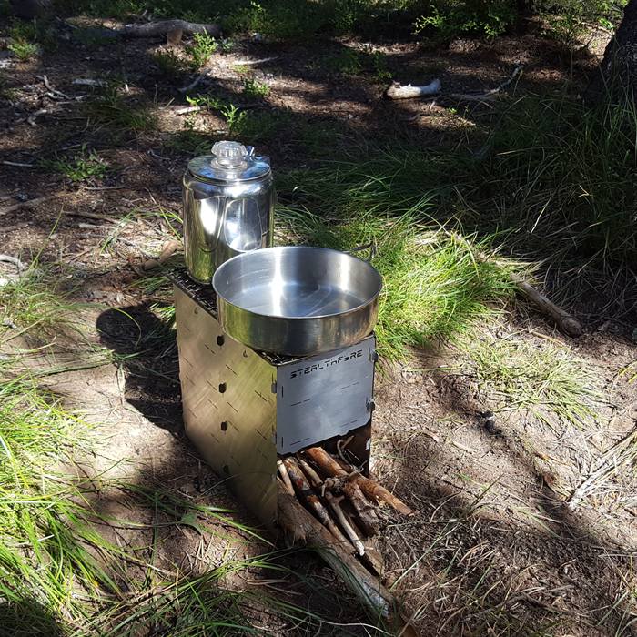 A frying pan and percolator side by side on the grill top of a StealthFyre stove burning wood