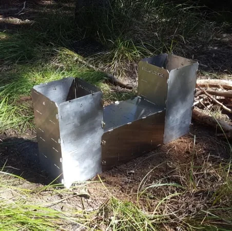 A StealthFyre Bush Runner assembled into an open stove on a forest floor, brand stamped on the stainless panel